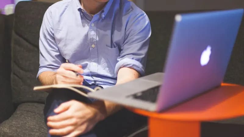 A person taking notes next to a laptop