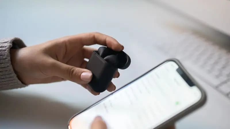 Person holding wireless earphones and a smartphone