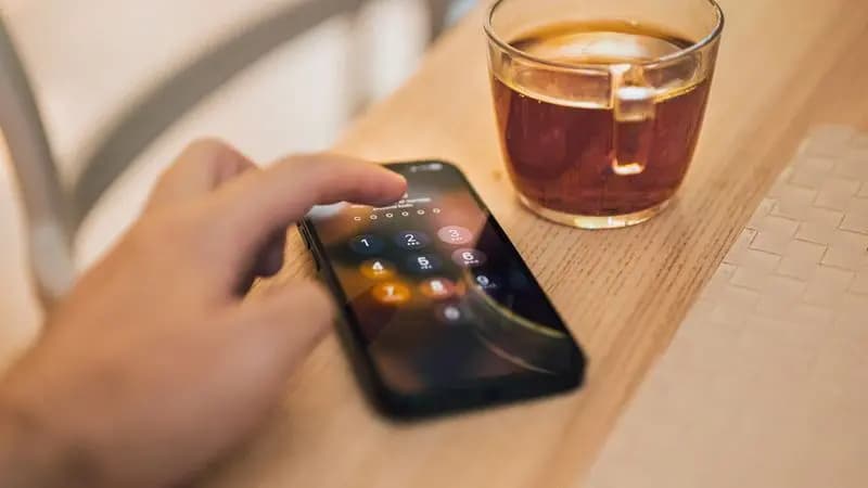 Hand unlocking an Android phone beside a cup of tea on a wooden table