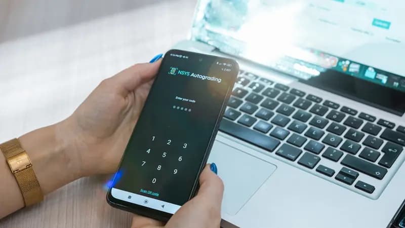 An Android phone showing a code entry screen with a keypad, held next to a laptop