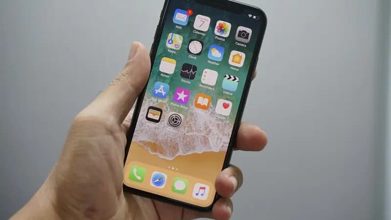 A hand holding an iPhone showing the home screen