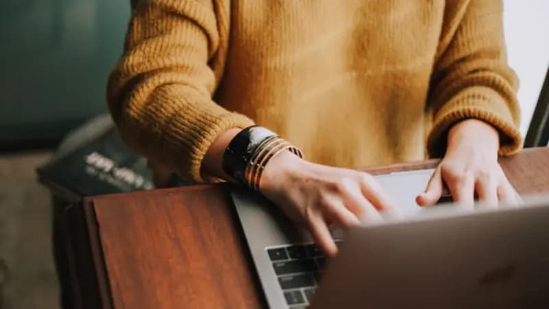 A person using a laptop at a wooden desk