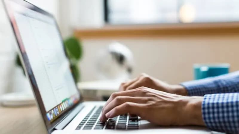 A person typing on a laptop by a window