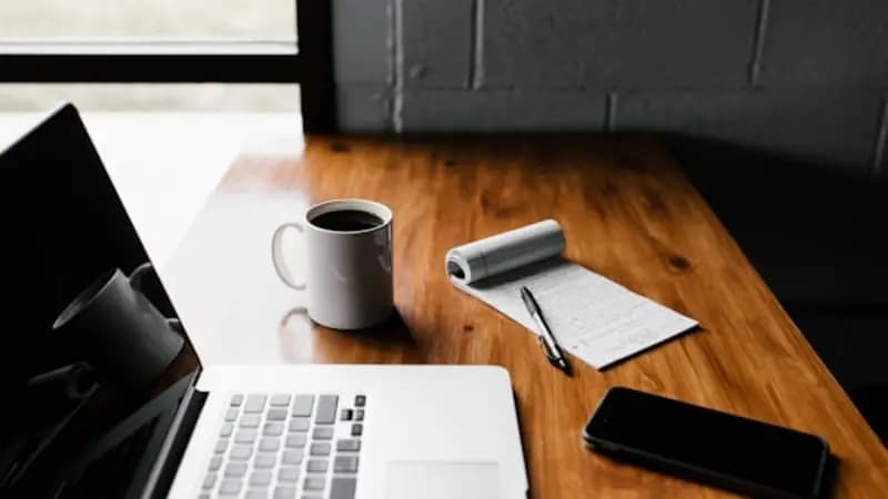 A laptop, coffee and a notepad on a wooden desk